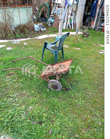 An iron cart and a plastic chair against the backdrop of a shed filled with junk and building materials 132294828