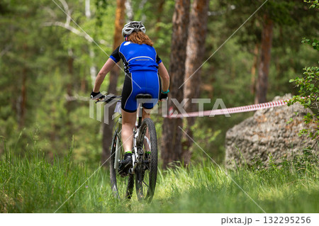 Rear view woman riding mountain bike in forest next to large rock Rear view woman riding mountain bike in forest next to large rock 132295256
