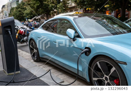 A plug-in sports car parked and connected to a charging station: the charging connector is highlighted. A concept for alternative mobility with a low environmental impact. A plug-in sports car parked and connected to a charging station: the charging connector is highlighted. A concept for alternative mobility with a low environmental impact. 132296043