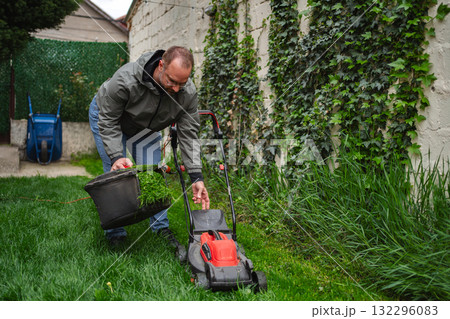 Lawn care expert meticulously collects clippings in a lush backyard during a bright afternoon 132296083