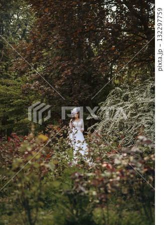 Elegant Bride in a Flowing White Gown Surrounded by Lush Greenery Elegant Bride in a Flowing White Gown Surrounded by Lush Greenery 132297759