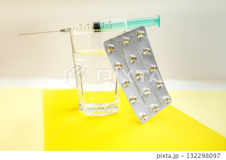Tablets in blister pack, syringe with vaccine and glass of water on yellow background. Tablets in blister pack, syringe with vaccine and glass of water on yellow background. 132298097