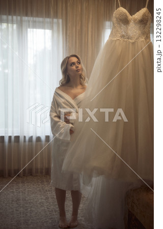 Beautiful girl looks at her wedding dress in a hotel room Beautiful girl looks at her wedding dress in a hotel room 132298245
