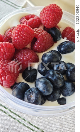 Close-up of fresh raspberries and blueberries served on creamy yogurt in a clear bowl 132298940