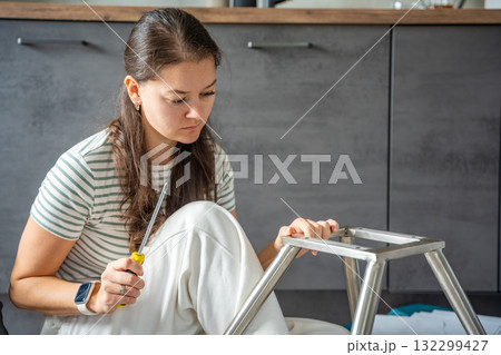 Young woman sitting on the floor assembling a chair with tools. Concept of female independence and do it yourself lifestyle. 132299427