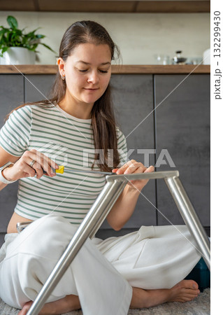 Smiling young woman assembling a chair with a screwdriver at home. Feminist concept celebrating female independence, confidence, and joy in do it yourself work. Smiling young woman assembling a chair with a screwdriver at home. Feminist concept celebrating female independence, confidence, and joy in do it yourself work. 132299430
