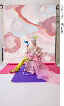 Elegant woman in Marie Antoinette character holding blue cocktail with feather garnish on abstract background. Elegant woman in Marie Antoinette character holding blue cocktail with feather garnish on abstract background. 132299568