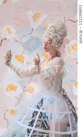 Playful rococo woman making selfie gesture with smartphone in floral studio Playful rococo woman making selfie gesture with smartphone in floral studio 132299601