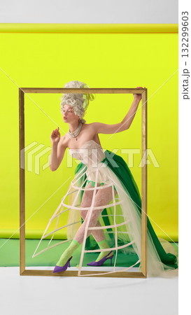 Elegant rococo woman in corset stepping through golden frame on yellow background Elegant rococo woman in corset stepping through golden frame on yellow background 132299603