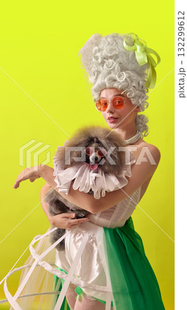 Stylish rococo woman with sunglasses holding fashionable poodle on yellow background 132299612