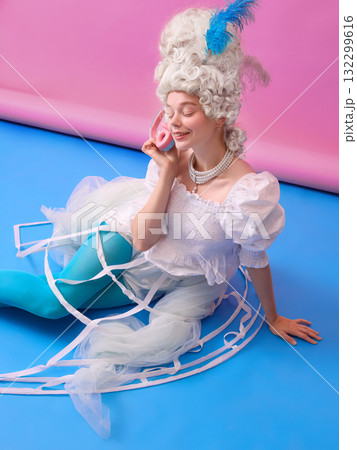 Smiling woman in white dress as Marie Antoinette with headphones on colorful background. 132299616