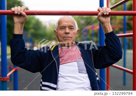 Elderly man pulls himself up on a horizontal bar on street sports field Elderly man pulls himself up on a horizontal bar on street sports field 132299784