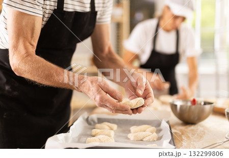 Close-up of baker hands placing pieces of raw dough on baking sheet in oven 132299806