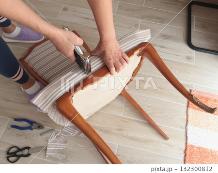 Anonymous person restore old vintage chair in home. Fabric replacement. Antique furniture and modern striped linen and cotton fabric. Hobbies, crafts, and retro-minimalist style. Anonymous person restore old vintage chair in home. Fabric replacement. Antique furniture and modern striped linen and cotton fabric. Hobbies, crafts, and retro-minimalist style. 132300812
