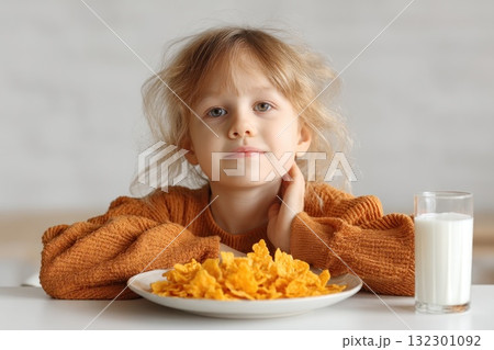 A girl sits at the table looking content as she enjoys cereal and a glass of milk during breakfast A girl sits at the table looking content as she enjoys cereal and a glass of milk during breakfast 132301092
