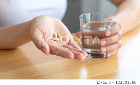 木製テーブルで薬を飲む女性の手元 木製テーブルで薬を飲む女性の手元 132301360