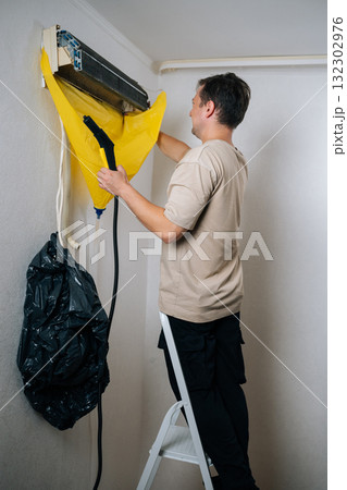 Vertical shot of technician male cleaning air conditioning unit using steam cleaner with protective sheet catching debris. Concept for maintenance of hygiene and pure air to prevent allergies 132302976