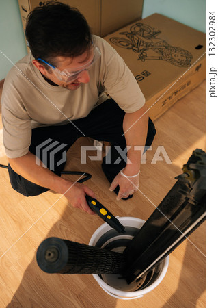 Cheerful repairman wearing safety glasses and gloves using a steam cleaner to clean air conditioner parts placed in bucket, ensuring proper hygiene and maintenance. Concept of air condition hygiene. 132302984