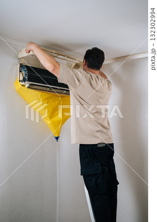 Vertical shot of HVAC technician carefully disassembling air conditioning unit, using protective bag to catch dripping water and debris during repair process. Concept of air condition maintenance. Vertical shot of HVAC technician carefully disassembling air conditioning unit, using protective bag to catch dripping water and debris during repair process. Concept of air condition maintenance. 132302994