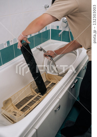 Close-up vertical shot of maintenance worker wearing protective gloves for thorough sanitization cleaning grimy air conditioner filter with shower head in bathtub. Concept of air condition hygiene. 132303003
