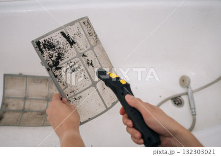 Closeup cropped shot of technician male using vacuum cleaner to remove dust and dirt from dirty air conditioner filter in bathroom, performing maintenance and improving air quality. 132303021