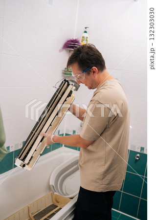 Cheerful professional HVAC technician man cleaning dirty air conditioner parts with detergent, ensuring proper hygiene and improved air quality. Concept of air condition maintenance service. 132303030