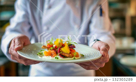 Professional chef presenting beautifully plated gourmet dish with colorful vegetables and artistic garnish in restaurant kitchen 132303289