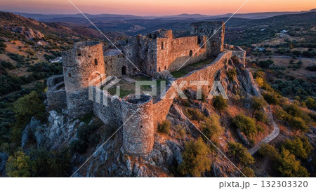 Ancient medieval castle ruins perched on rocky hilltop during golden sunset with rolling countryside landscape stretching into distance Ancient medieval castle ruins perched on rocky hilltop during golden sunset with rolling countryside landscape stretching into distance 132303320