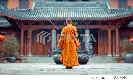 Buddhist monk in traditional orange robes walking toward ornate Asian temple with curved roof tiles and intricate architectural details in serene courtyard setting 132303403
