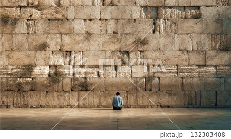 Solitary person sitting in contemplation before massive ancient stone wall, showcasing scale and historical architecture in peaceful moment 132303408
