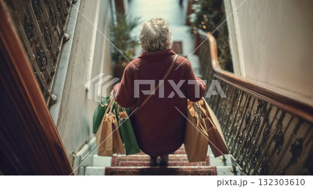 Senior woman carrying shopping bags walking up stairs in residential building during holiday season with festive decorations visible Senior woman carrying shopping bags walking up stairs in residential building during holiday season with festive decorations visible 132303610