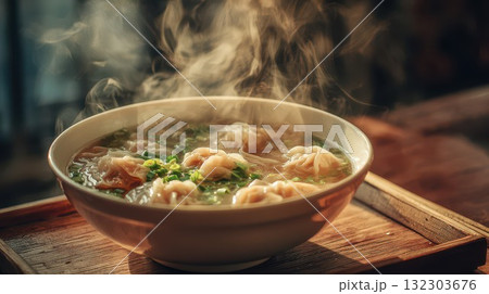 Steaming hot wonton soup with dumplings in clear broth, garnished with green onions and herbs. Asian comfort food in white bowl with chopsticks nearby Steaming hot wonton soup with dumplings in clear broth, garnished with green onions and herbs. Asian comfort food in white bowl with chopsticks nearby 132303676