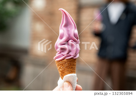 Soft serve ice cream cone with a purple swirl held in a hand on a sunny day Soft serve ice cream cone with a purple swirl held in a hand on a sunny day 132303894