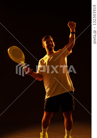 Man celebrating victory with a paddle racket in a dramatic lighting setup 132303919