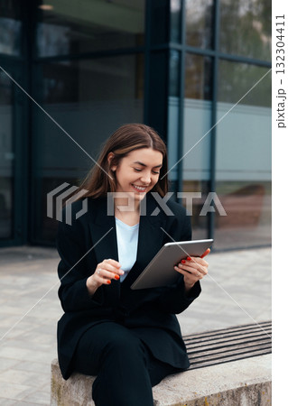 Woman Using Tablet While Sitting on Bench Outside Modern Building During Daytime 132304411