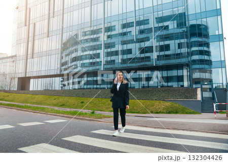 Woman Walking Across a Crosswalk Near a Modern Glass Building in an Urban Setting During Daylight Hours Woman Walking Across a Crosswalk Near a Modern Glass Building in an Urban Setting During Daylight Hours 132304426