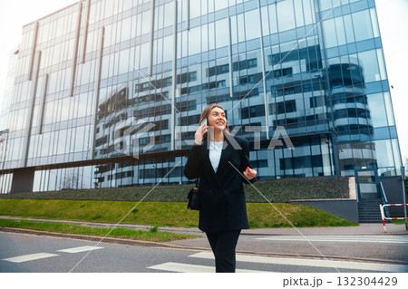 Confident Businesswoman Walking Along the City Sidewalk in Front of a Modern Glass Building During a Sunny Day Confident Businesswoman Walking Along the City Sidewalk in Front of a Modern Glass Building During a Sunny Day 132304429