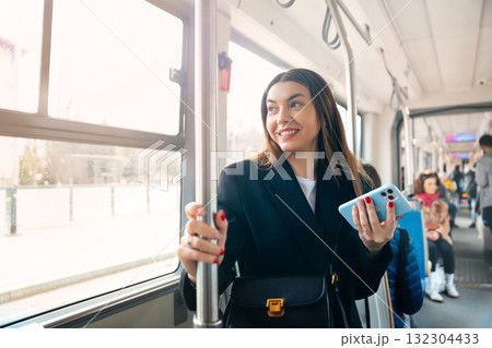 Woman Riding Public Transport Holding a Smartphone and Smiling During Daylight in a Modern Urban Environment Woman Riding Public Transport Holding a Smartphone and Smiling During Daylight in a Modern Urban Environment 132304433