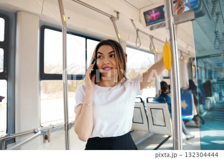 Young Woman Talking on Phone While Standing Inside a Public Transport Vehicle During Daytime and Enjoying Her Commute Young Woman Talking on Phone While Standing Inside a Public Transport Vehicle During Daytime and Enjoying Her Commute 132304444