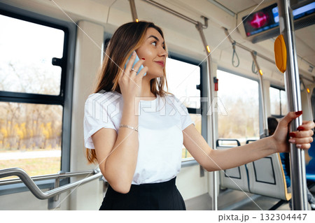 Young Woman on Public Transport Talking on Phone While Standing in a Modern Tram During Daylight Hours 132304447