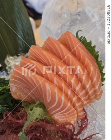 Fresh salmon sashimi served on ice with garnishes, showcasing vibrant colors and textures. This dish highlights delicate layers of fish, perfect for sushi lovers 132308816