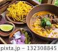 Delicious bowl of curry noodles with tender meat, crispy fried noodles, and fresh garnishes, served with lime and pickled vegetables for flavorful meal 132308845