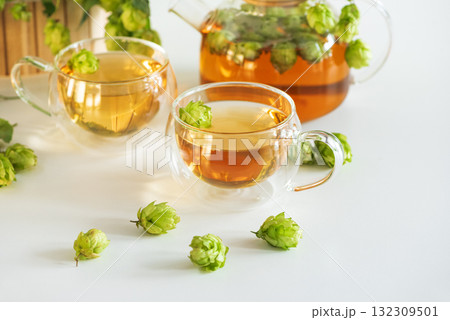 Hop Tea in Glass Teapot and Cups with Fresh Hops on Table 132309501
