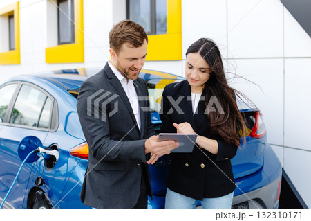 Smiling woman standing at the car and pointing at car seller tablet. She is picked right car for her she saw online. A woman concludes an agreement to buy a car and shakes the manager's hand Smiling woman standing at the car and pointing at car seller tablet. She is picked right car for her she saw online. A woman concludes an agreement to buy a car and shakes the manager's hand 132310171