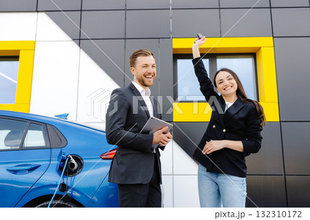 Happy female client standing at brand new car and taking keys from dealer in dealership outdoor. The woman is very happy with the new car, holding the keys in her hands Happy female client standing at brand new car and taking keys from dealer in dealership outdoor. The woman is very happy with the new car, holding the keys in her hands 132310172