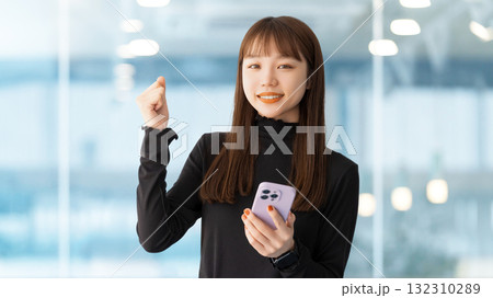 スマートフォンを持ってガッツポーズをする女性・ビジネスウーマン スマートフォンを持ってガッツポーズをする女性・ビジネスウーマン 132310289