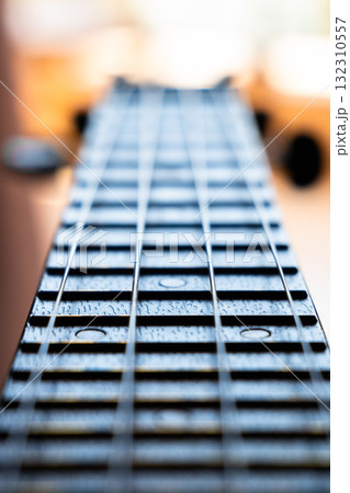 Close-up of a guitar fretboard with wooden texture and metal strings. The background is softly blurred, highlighting the instrument's details.	 132310557