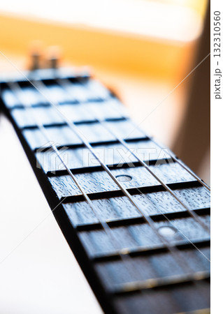 Close-up of a guitar fretboard with wooden texture and metal strings. The background is softly blurred, highlighting the instrument's details.	 132310560