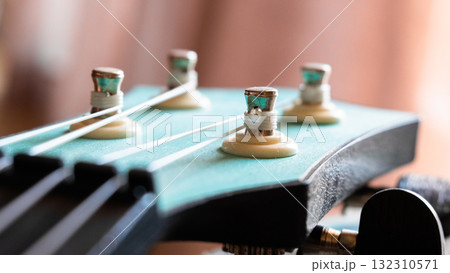 Close-up of a guitar headstock with tuning pegs and strings. The headstock is turquoise with metallic components. The background is softly blurred. Close-up of a guitar headstock with tuning pegs and strings. The headstock is turquoise with metallic components. The background is softly blurred. 132310571