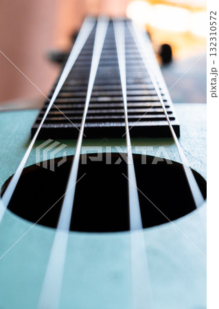 Close-up of a guitar fretboard with wooden texture and metal strings. The background is softly blurred, highlighting the instrument's details. Close-up of a guitar fretboard with wooden texture and metal strings. The background is softly blurred, highlighting the instrument's details. 132310572